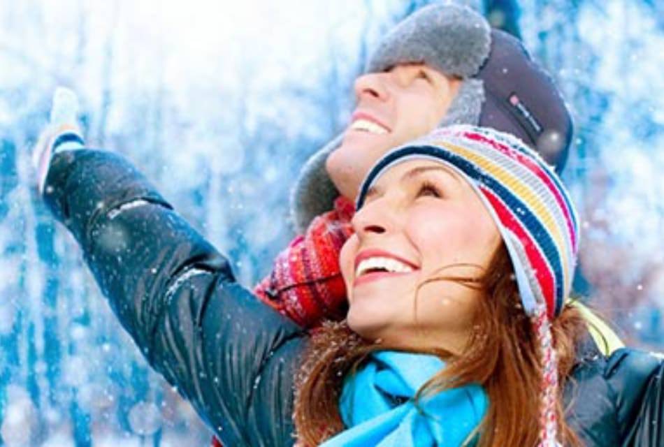 Happy couple dressed in winter outdoor clothing look up at snow falling.