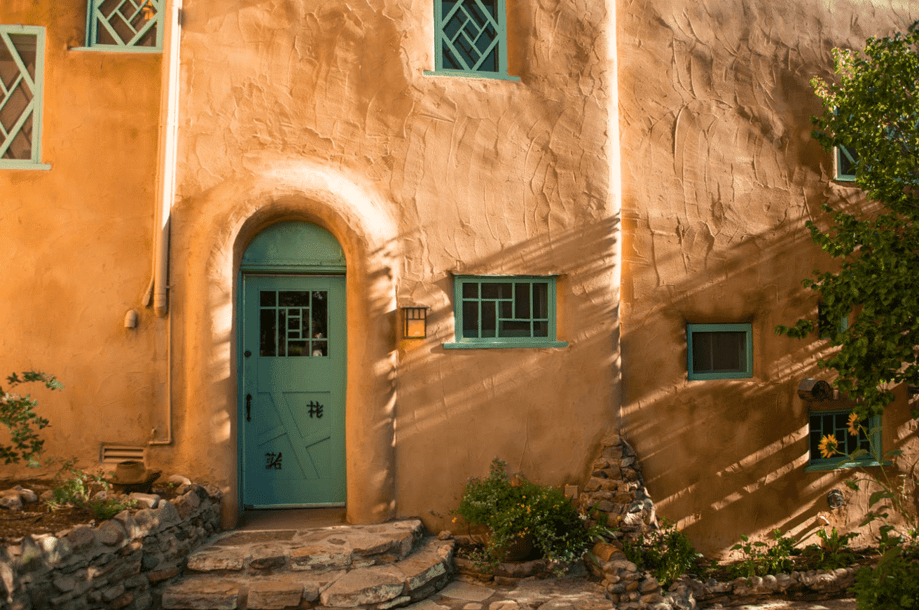 Exterior view of Inn of the Turquoise Bear with clay colored adobe and turquoise trim and front door|O Henry guest room queen bed
